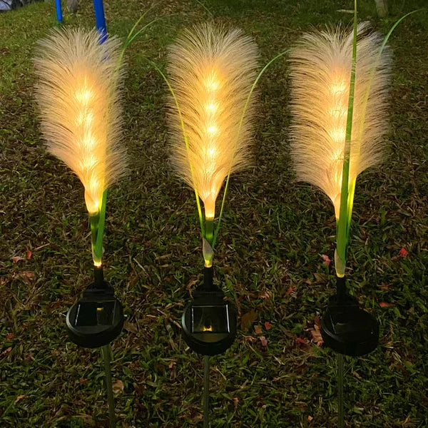 Drei leuchtende LED-Solar-Gartenleuchten in Federform auf Rasen bei Nacht.