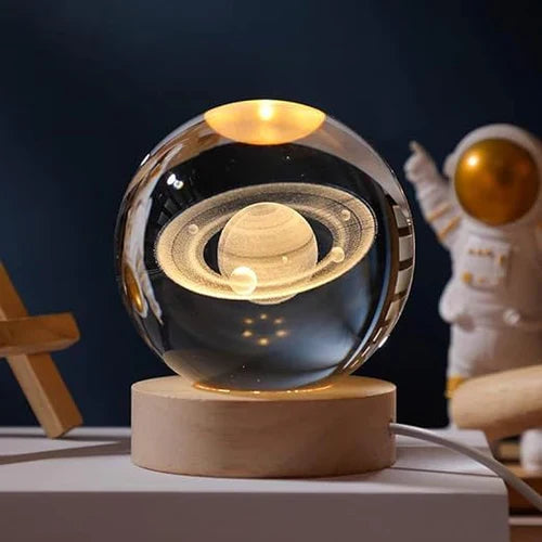 Kristallkugel mit Saturn-Design auf Holzsockel, dekorative LED-Lampe, Astronaut im Hintergrund.