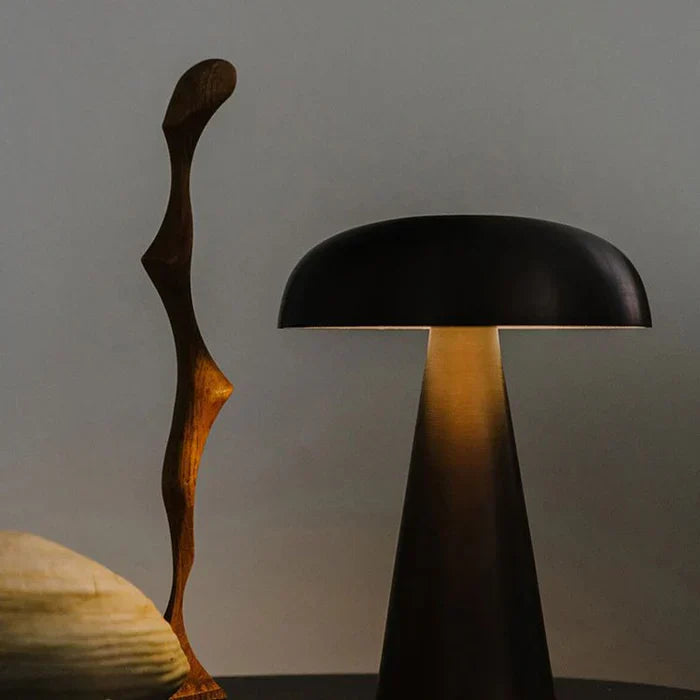 Schwarze Tischlampe aus Metall, modern, neben Holzskulptur auf dunklem Tisch.