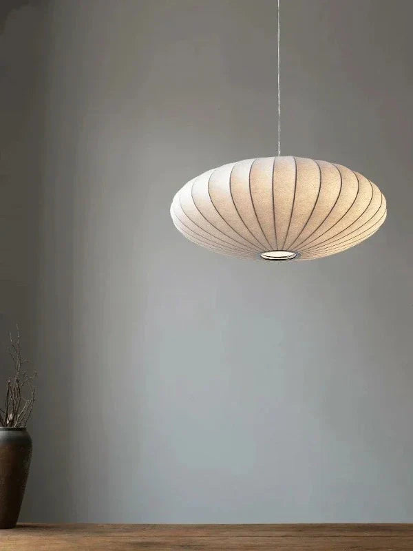 Moderne weiße Pendelleuchte aus Stoff, hängend über einem Holztisch, minimalistisches Design.