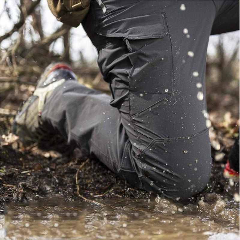 Wasserdichte Outdoor-Hose in Grau, kniend im Schlamm, ideal für Trekking und Wandern.