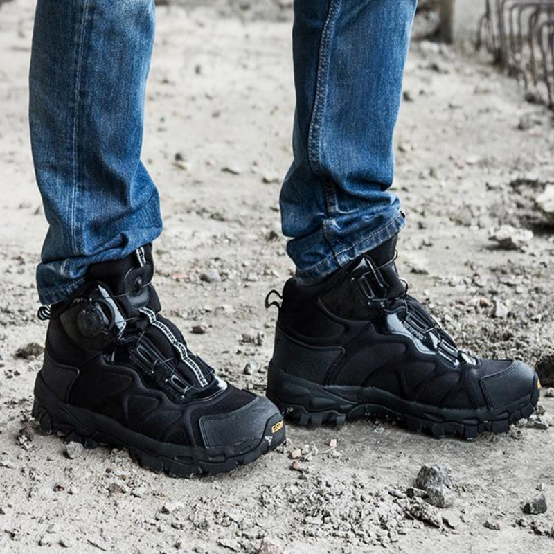 Schwarze Outdoor-Wanderschuhe, robustes Design, getragen mit blauen Jeans, auf steinigem Untergrund.