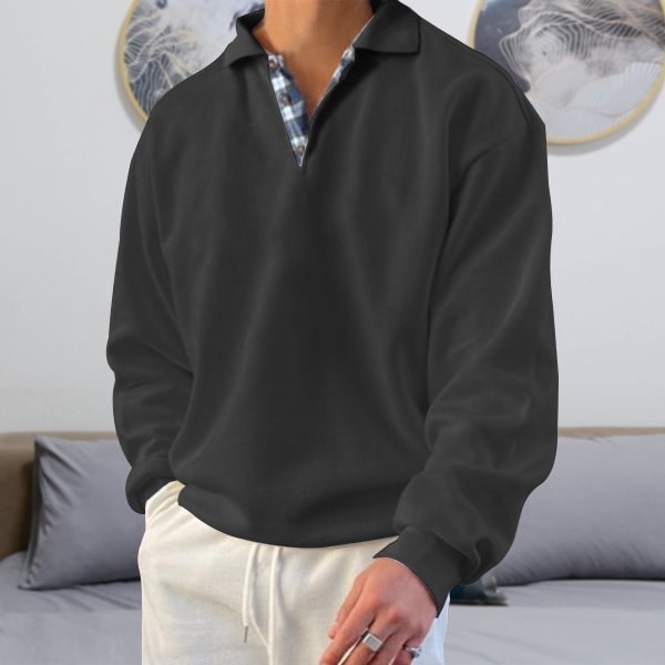 Schwarzer Herrenpullover mit Kragen, kariertes Hemd darunter, lässiger Stil, Wohnzimmer-Hintergrund.