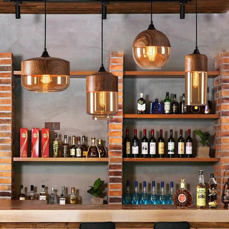 Drei hängende Holz-Kupfer-Pendelleuchten über einer Bar mit Spirituosenflaschen im Hintergrund.