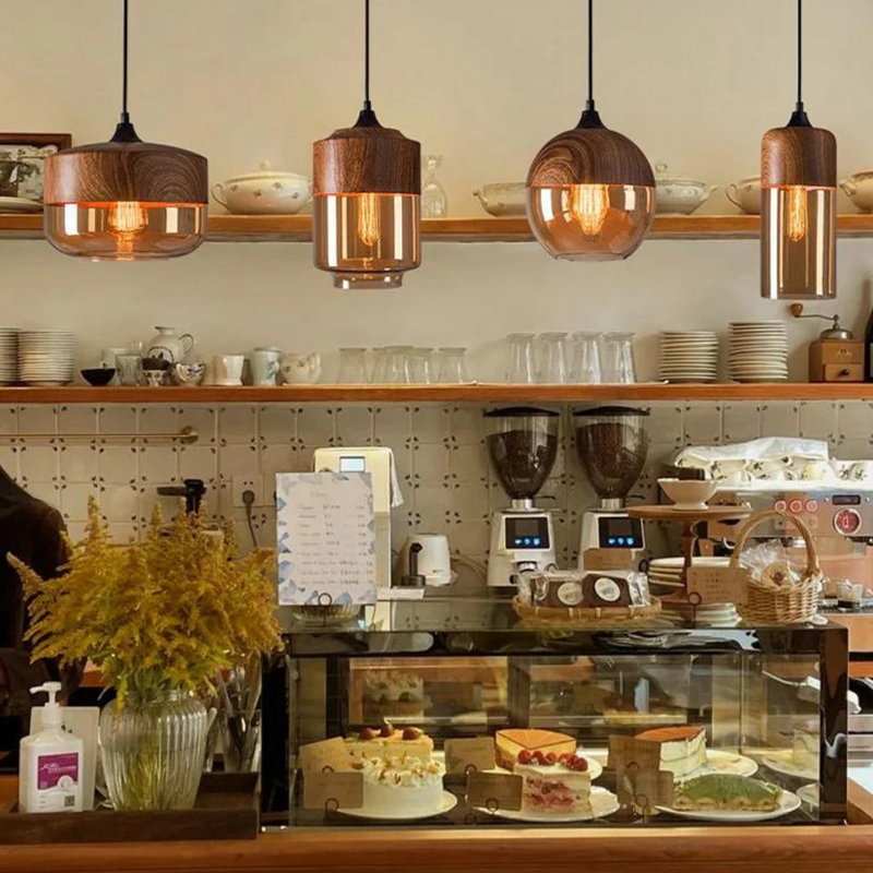 Café-Theke mit Kuchen, Holzlampen, Blumen, Kaffeemaschinen und Geschirr im Hintergrund.