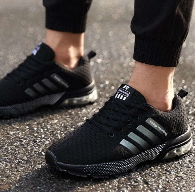 Schwarze Herren-Laufschuhe mit reflektierenden Streifen, atmungsaktiv, auf nasser Straße.