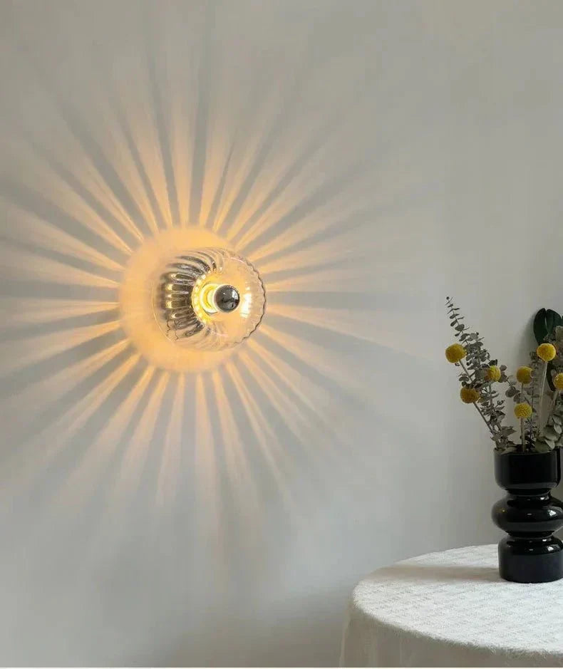Wandlampe aus Glas, strahlt warmes Licht, modernes Design, neben Tisch mit Vase, minimalistisch.