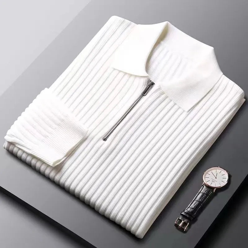 Zusammengelegter weißer Strickpullover mit Reißverschluss und Armbanduhr auf grauem Hintergrund.