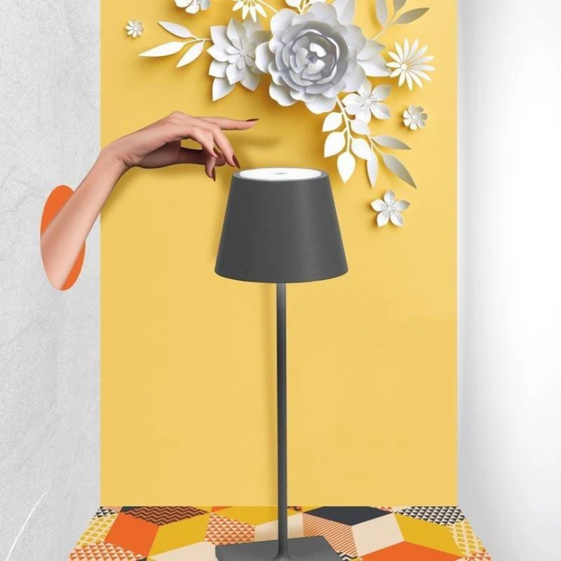 Graue Tischlampe mit schwarzem Schirm, gelber Hintergrund, dekorative Papierblumen.