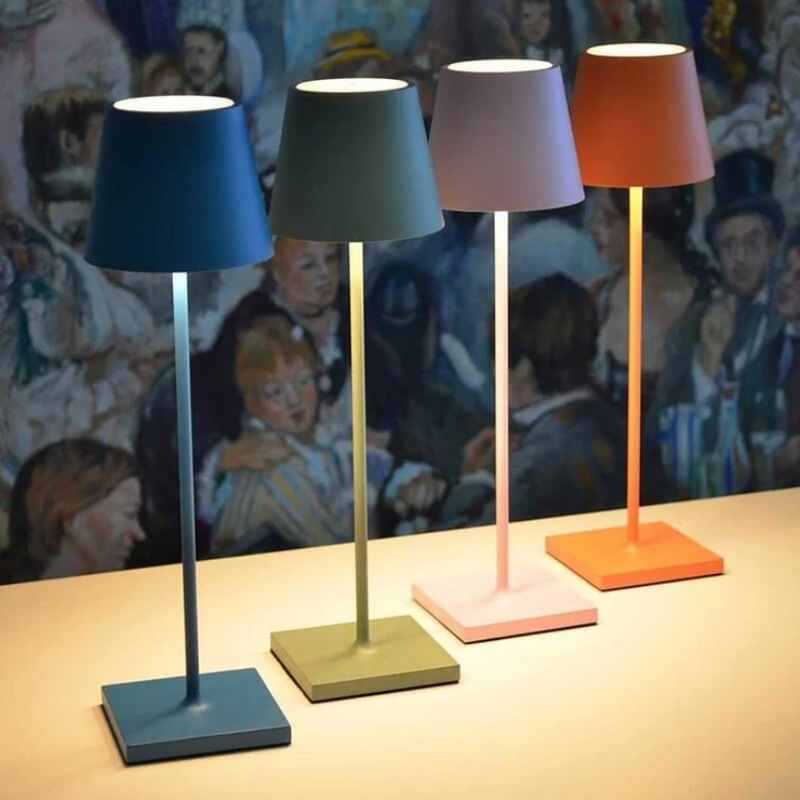 Vier bunte Tischlampen in Blau, Grün, Rosa und Orange auf einem Tisch vor einem Gemälde.
