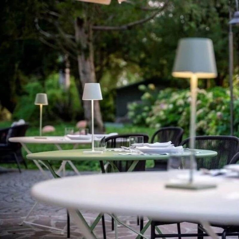 Grüner Gartentisch mit weißer Tischlampe, umgeben von Stühlen im Freien, Naturhintergrund.