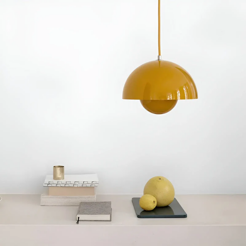 Gelbe Pendelleuchte aus Metall über modernem Tisch mit Büchern und Früchten, skandinavisches Design.