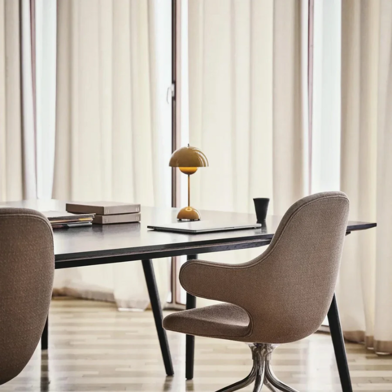 Brauner Bürostuhl und Tisch mit gelber Lampe, modernes Bürodesign, Holzboden, helle Vorhänge.