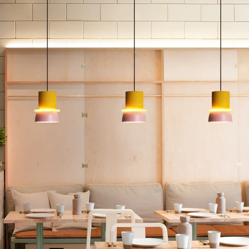 Drei bunte Pendelleuchten über Esstischen in modernem Café-Interieur.