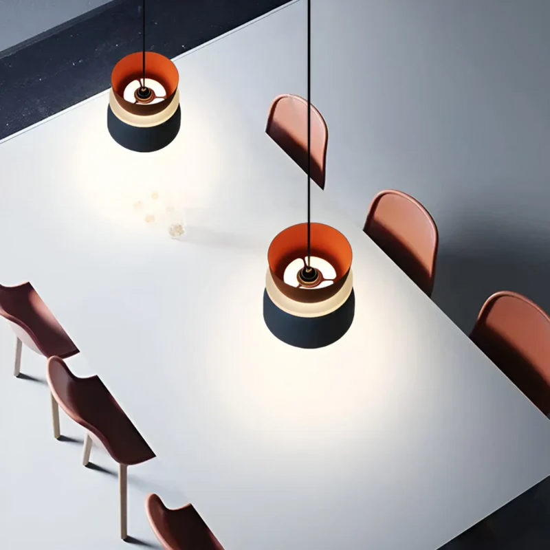 Moderne Esszimmerbeleuchtung, schwarze und orangefarbene Pendelleuchten über weißem Tisch.