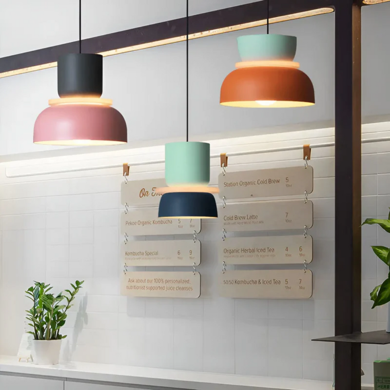 Moderne Hängelampen in Schwarz, Rosa, Türkis und Orange über einer Café-Theke.