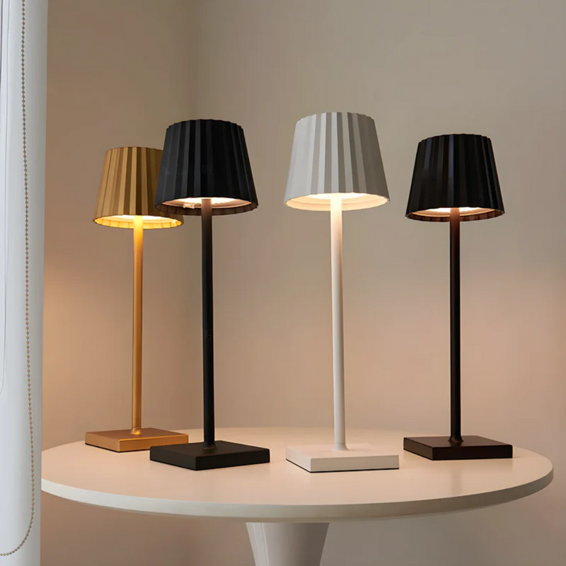 Vier moderne Tischlampen in Gold, Schwarz, Weiß und Braun auf rundem Tisch, elegantes Design.