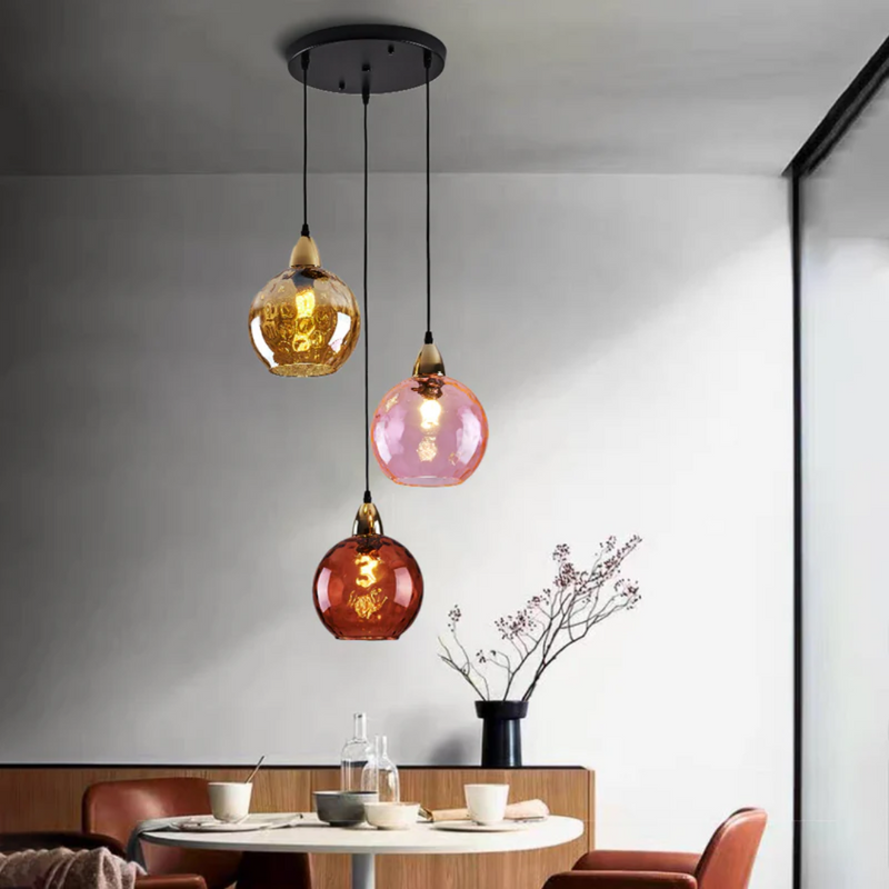 Dreifache Pendelleuchte aus Glas in Bernstein, Rosa und Rot über Esstisch, modernes Design.