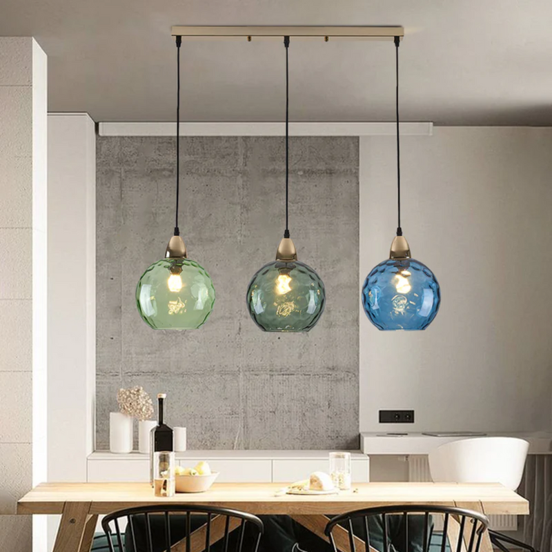 Drei bunte Glas-Pendelleuchten über Esstisch in modernem Esszimmer, stilvolle Beleuchtung.
