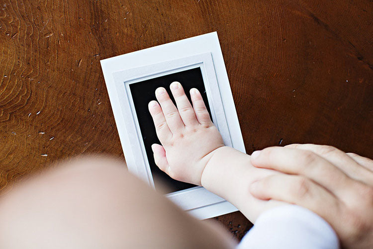 Babyhand auf Tintenpad für Handabdruck, Holzuntergrund, DIY-Erinnerung, weißes Papier.
