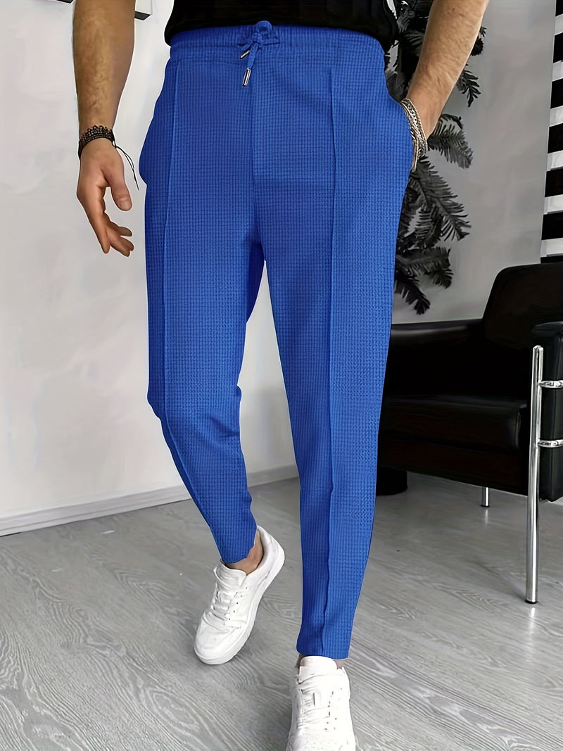 Mann in blauer Jogginghose und weißen Sneakers im modernen Wohnzimmer.