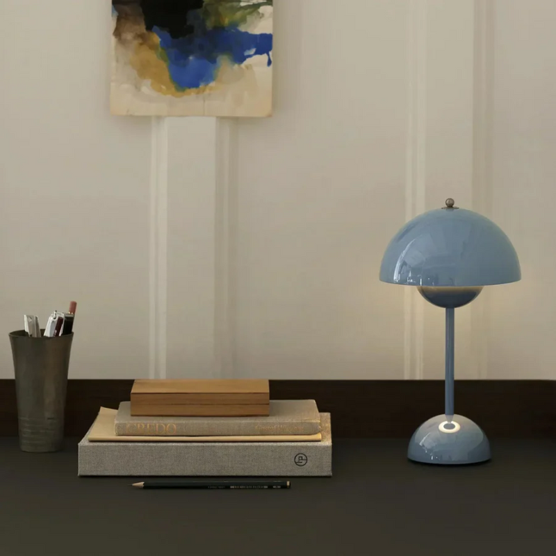 Blaue Tischlampe auf Schreibtisch mit Büchern, Stiftehalter und abstraktem Wandbild.