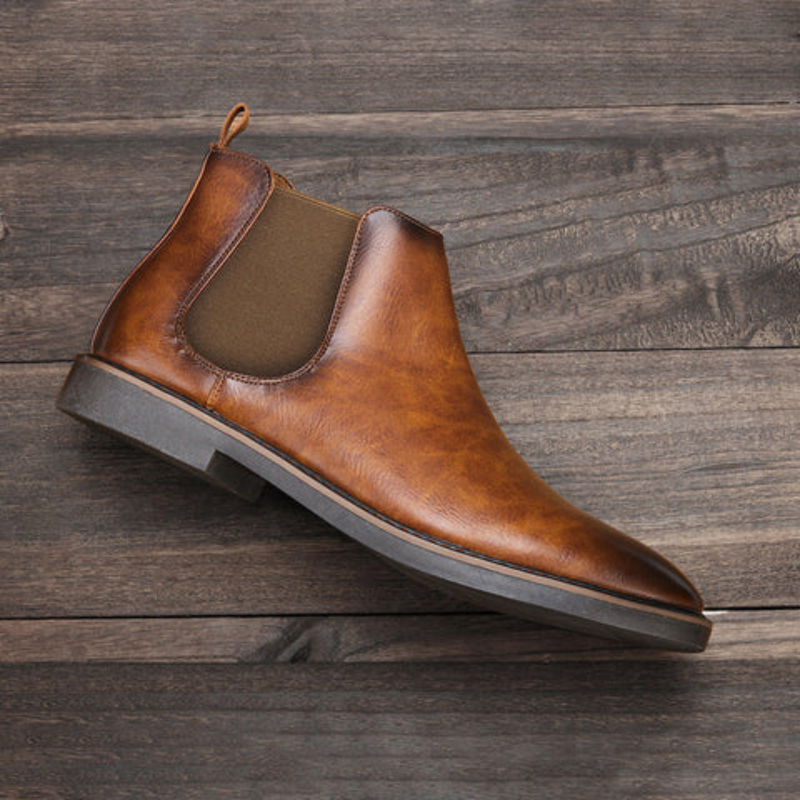 Brauner Leder-Chelsea-Boot für Herren, elegantes Design, rutschfeste Sohle, Holzboden-Hintergrund.