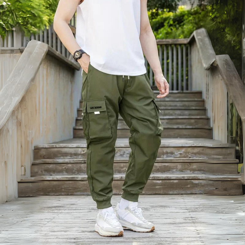 Mann in Armeegrüner Cargohose, weißem T-Shirt, Treppe, lässiger Stil, Outdoor-Mode.