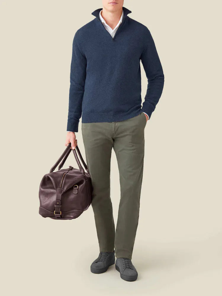 Mann in blauem Kaschmir-Pullover mit Reißverschluss, olivgrüner Hose, brauner Ledertasche.
