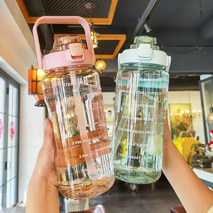 Zwei große Wasserflaschen, rosa und grün, mit Motivationsaufdruck, im modernen Café.