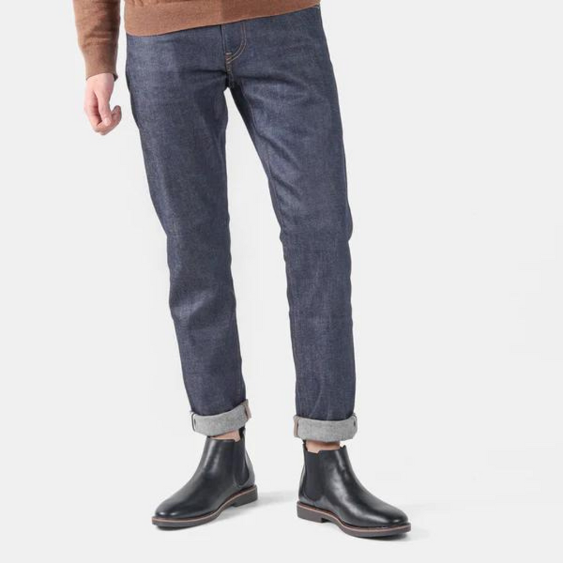 Mann in blauer Jeans und schwarzen Chelsea Boots aus Leder auf weißem Hintergrund.