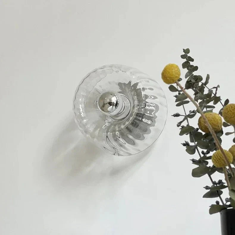 Glasvase mit Metallknauf, transparent, dekorativ, neben gelben Blumen und Eukalyptuszweigen.