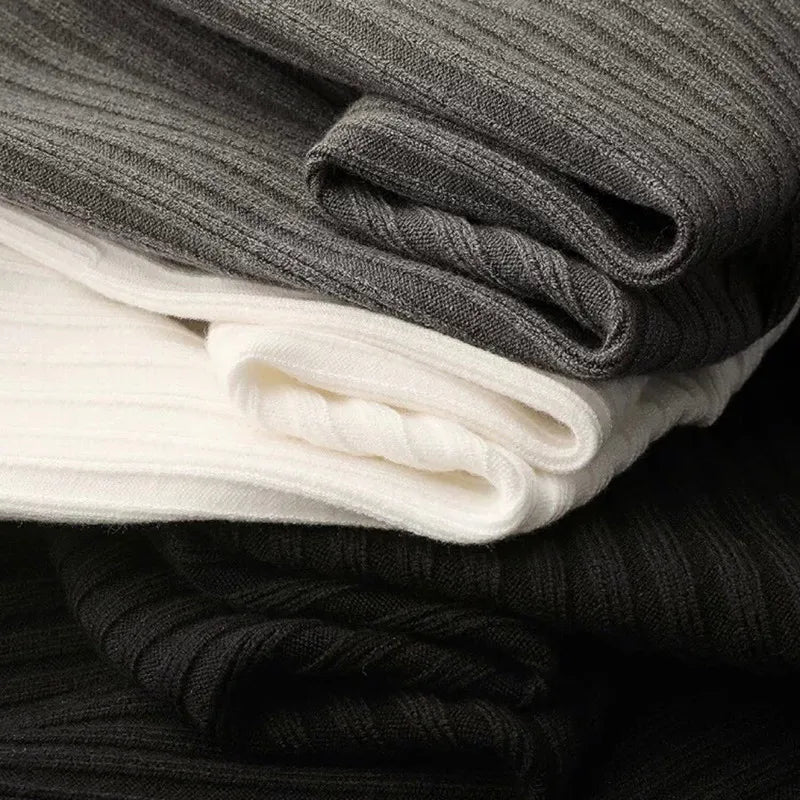 Gefaltete Strickstoffe in Schwarz, Weiß und Grau, gerippt, weiche Textur, hochwertige Materialien.
