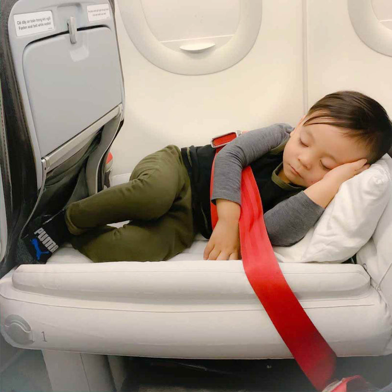 Kleinkind schläft auf Flyaway Kids Bed im Flugzeug, roter Sicherheitsgurt, bequeme Reise.