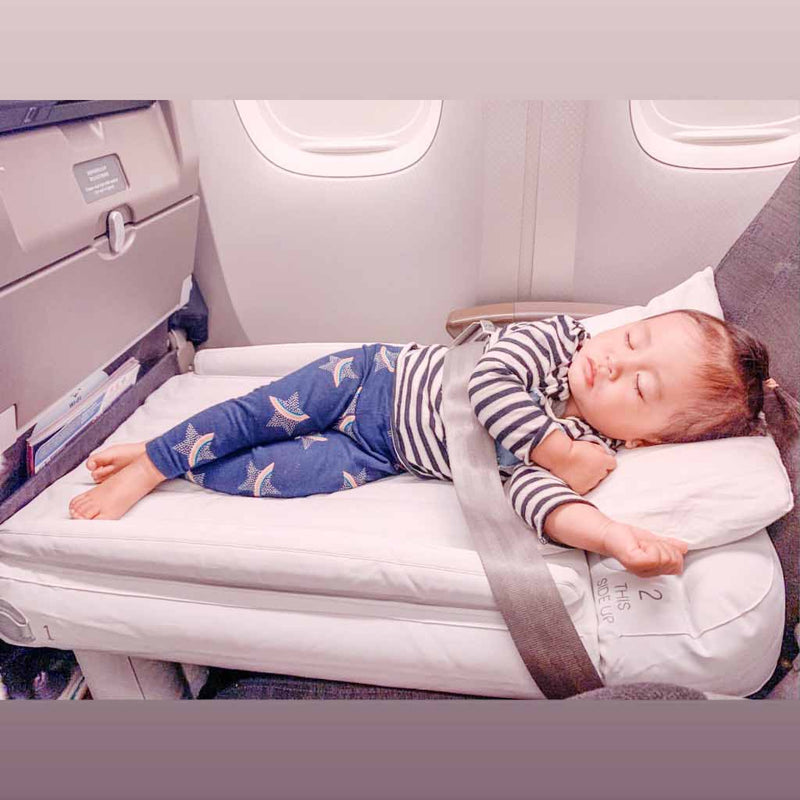 Kleinkind schläft auf aufblasbarem Flugzeugbett, gestreiftes Shirt, blaue Hose, Flugreise.