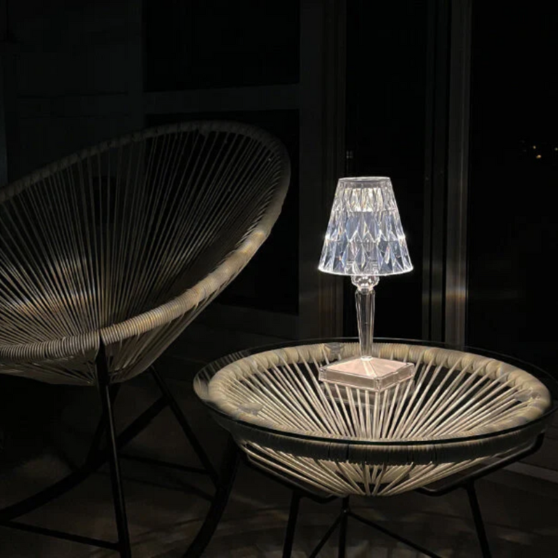 Transparente Kristalllampe auf rundem Tisch, moderne Gartenmöbel, Nachtaufnahme.