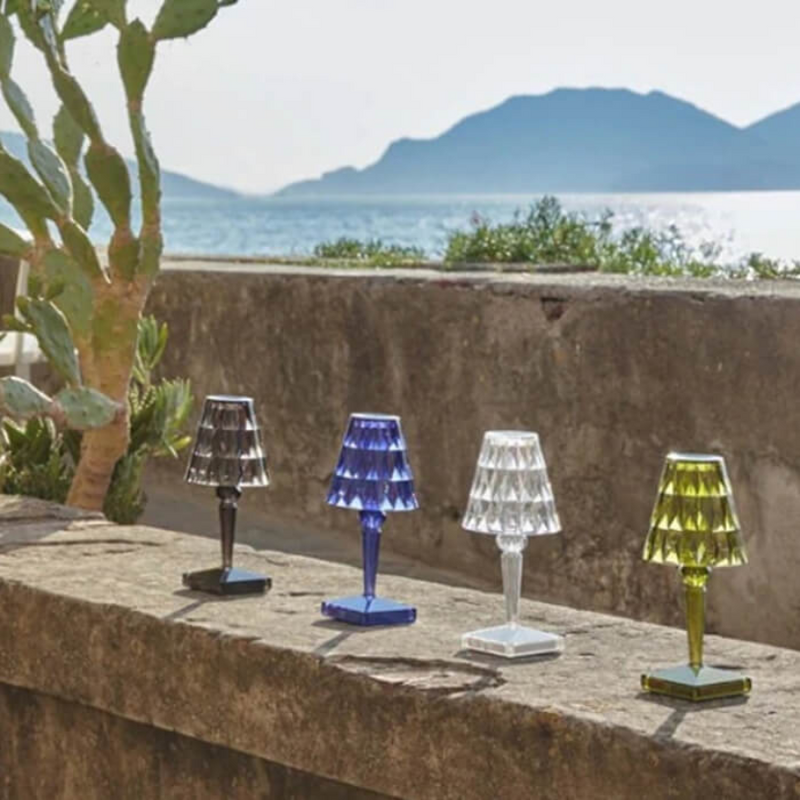 Vier bunte Kristall-Tischlampen auf Steinmauer vor Meer und Bergen im Hintergrund.