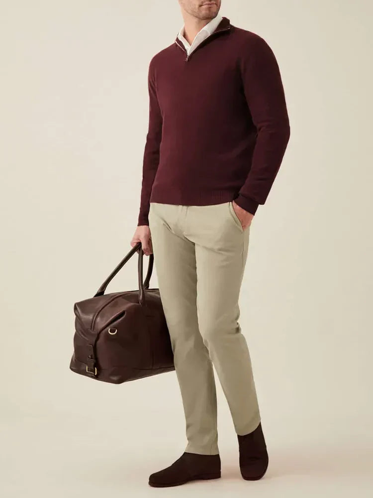 Mann in bordeauxrotem Kaschmirpullover, beige Hose, braune Tasche, braune Schuhe.