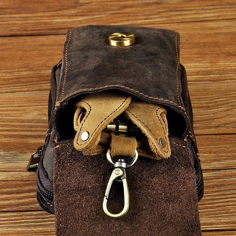 Braune Herren-Gürteltasche aus Leder mit Karabinerhaken auf Holzhintergrund.