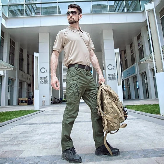 Mann in taktischer Kleidung mit Rucksack vor modernem Gebäude, Outdoor-Ausrüstung, urbaner Stil.