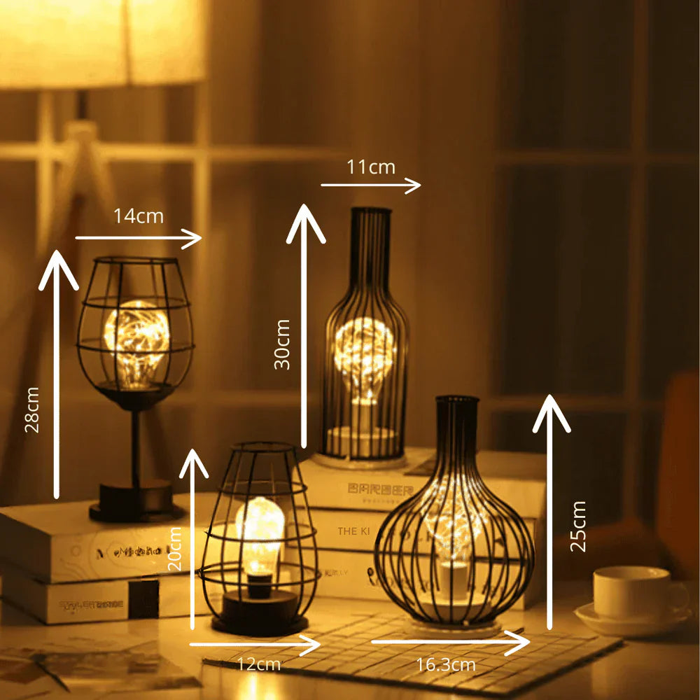 Vier dekorative LED-Lampen in schwarzem Metallkäfig-Design auf einem Tisch, warmes Licht.