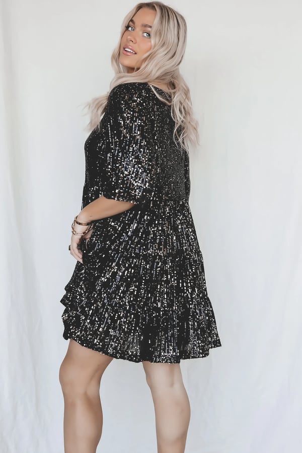 Frau in schwarzem Paillettenkleid, blondes Haar, modisches Abendoutfit, glamouröses Design.