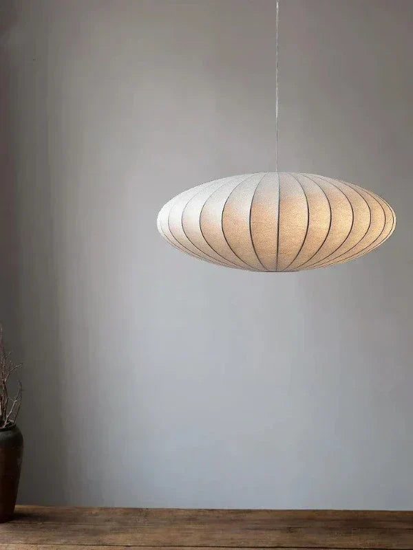 Moderne weiße Pendelleuchte aus Stoff, oval, hängend über Holztisch, minimalistisches Design.