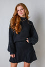 Junge Frau in schwarzem Strickpullover und Faltenrock, lächelnd, modisch, Herbstmode.