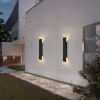 Moderne schwarze Außenwandleuchten an weißer Hauswand, beleuchteter Gartenweg.