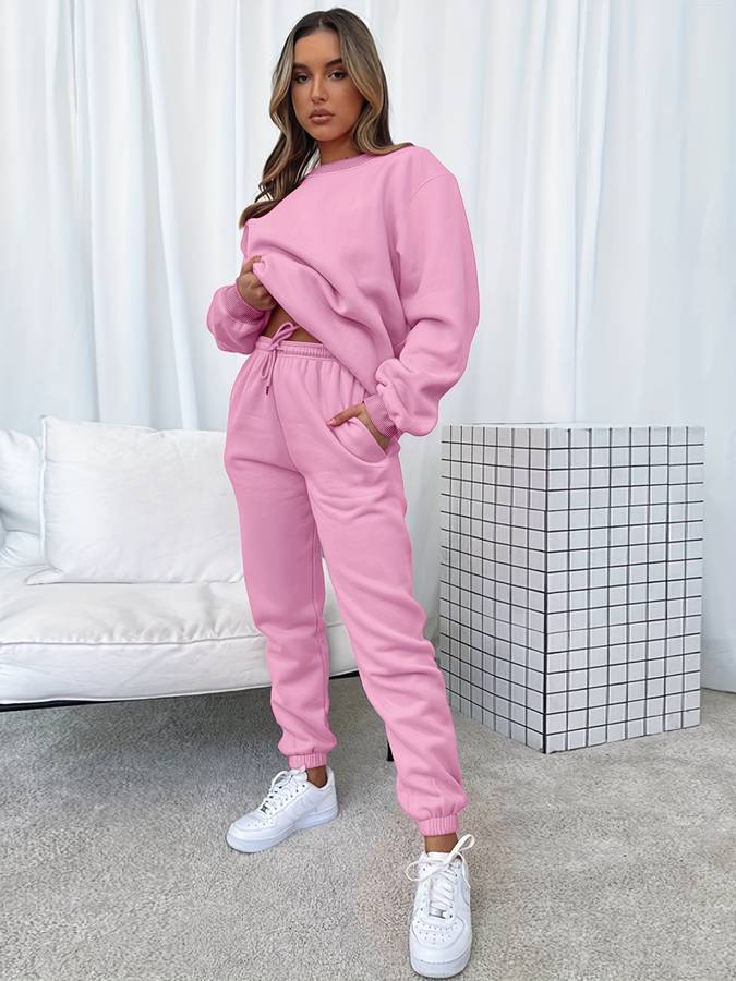Frau in rosa Jogginganzug, weiße Sneaker, modernes Wohnzimmer, gemütliche Mode, Freizeitkleidung.