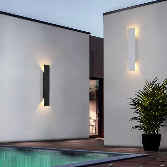 Moderne schwarze Außenwandleuchte an weißer Hauswand neben Pool bei Dämmerung.
