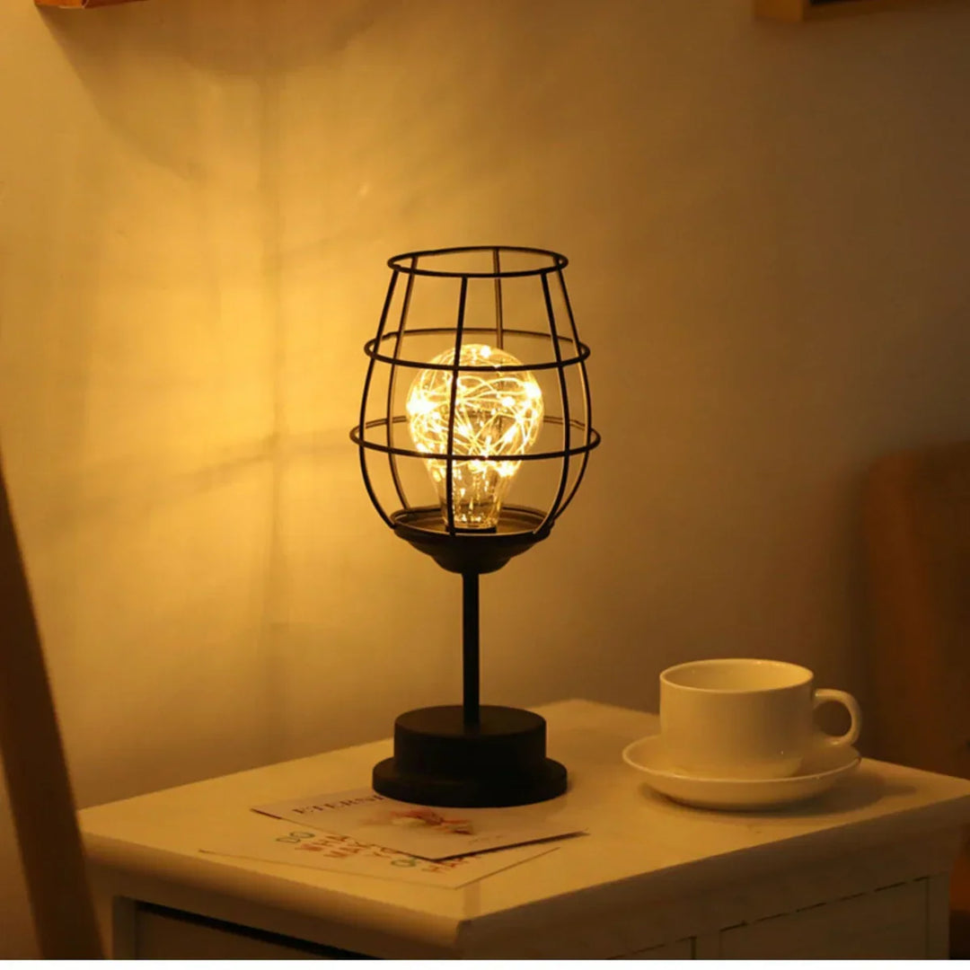 Schwarze Tischlampe mit Gitterdesign, warmes Licht, auf weißem Nachttisch neben Kaffeetasse.