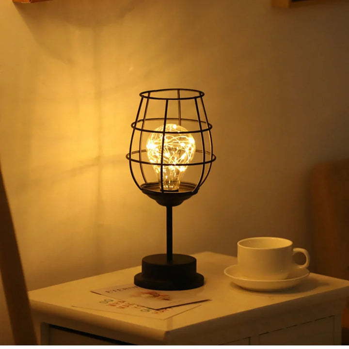Schwarze Tischlampe mit Gitterdesign, warmes Licht, auf weißem Nachttisch neben Kaffeetasse.