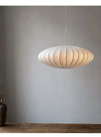 Moderne weiße Pendelleuchte aus Stoff, oval, hängend über Holztisch, minimalistisches Design.